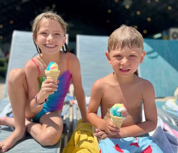 Two children holding rainbow-swirled ice cream cones by poolside lounge chairs at Splash RV Resort in Milton, Florida