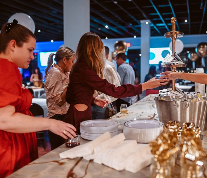 Splash RV Resort in Milton, Florida: elegantly dressed guests gather at marble bar with champagne flutes, moody blue lighting, twinkling ceiling lights, gold and white balloons.