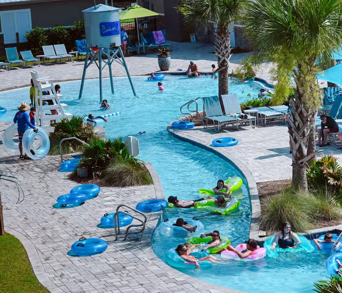 Guests floating on tubes along a winding lazy river at Splash RV Resort, surrounded by palm trees and luxury cottages.