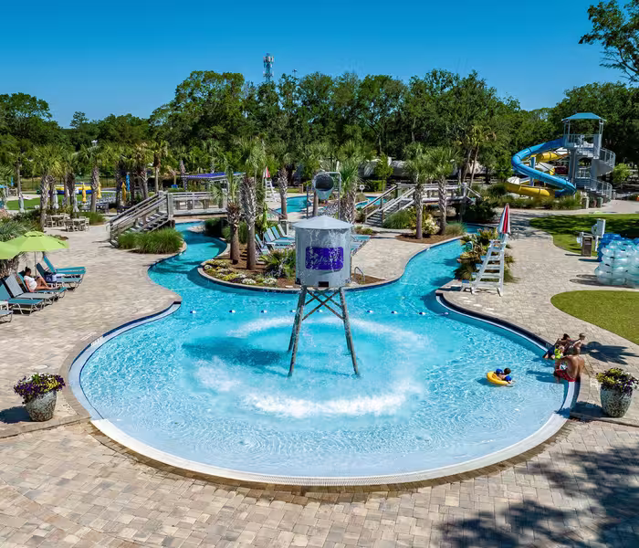 Guests float on tubes in the lazy river at Splash RV Resort, featuring a large tipping bucket and water slide.