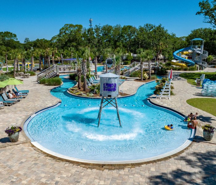 Guests float on tubes in the lazy river at Splash RV Resort, featuring a large tipping bucket and water slide.