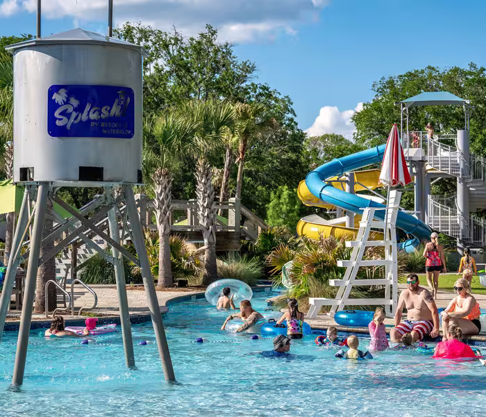 Guests float on tubes in the lazy river near a blue and yellow water slide at Splash RV Resort.