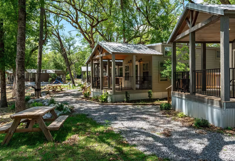 Luxury cottages with covered porches and metal roofs nestled among trees at Splash RV Resort.
