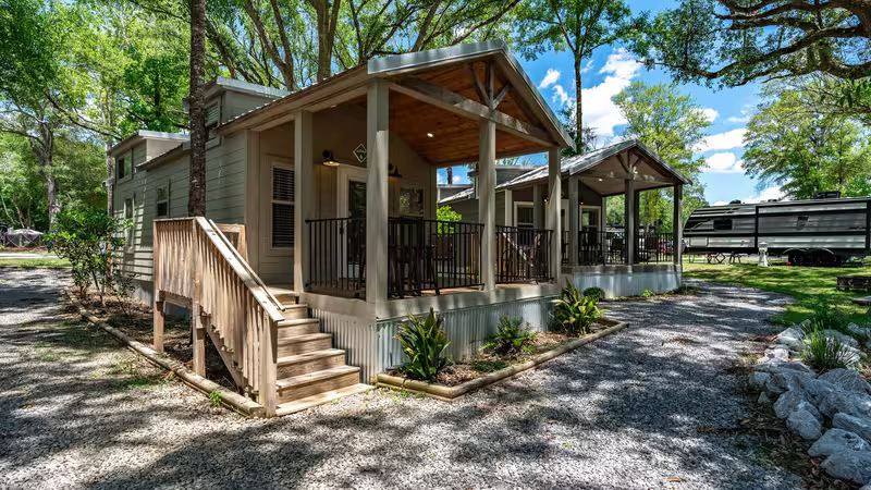Sage-green luxury cottages with covered porches and wooden stairs at Splash RV Resort.