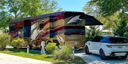 Luxury motorhome parked at Splash RV Resort with a white SUV and manicured landscaping.