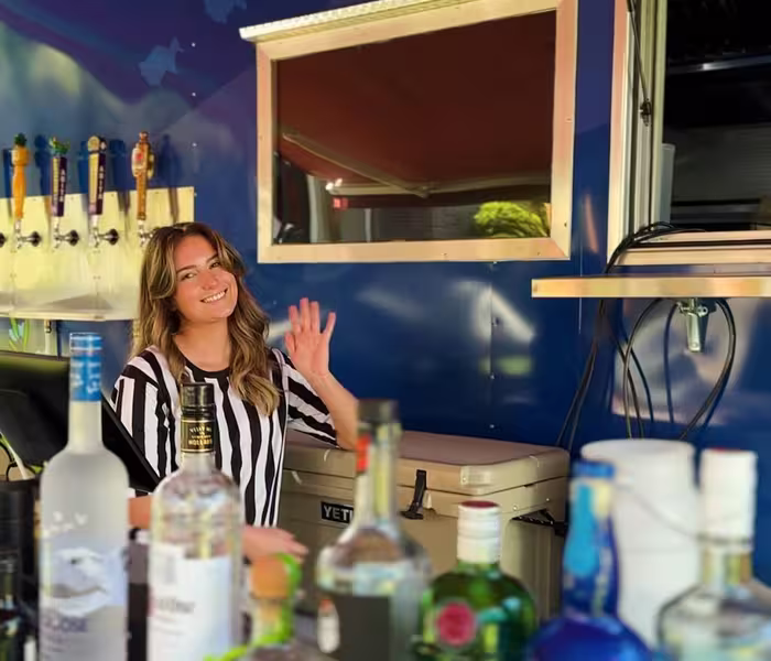 Smiling bartender waves from a mobile bar cart stocked with drinks at Splash RV Resort.