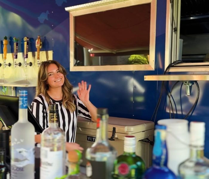 Smiling bartender waves from a mobile bar cart stocked with drinks at Splash RV Resort.