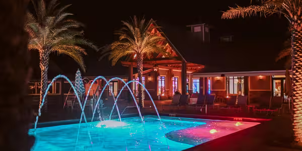 Glowing blue swimming pool with arched fountains at Splash RV Resort at night.