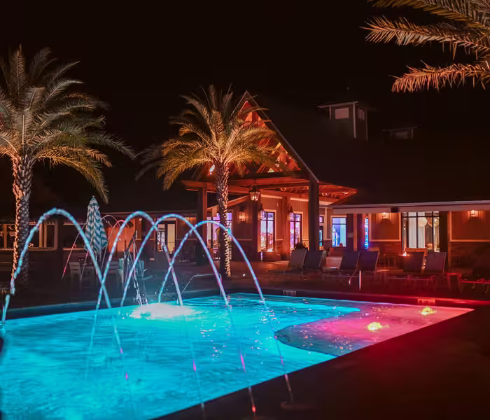 Glowing blue swimming pool with arched fountains at Splash RV Resort at night.