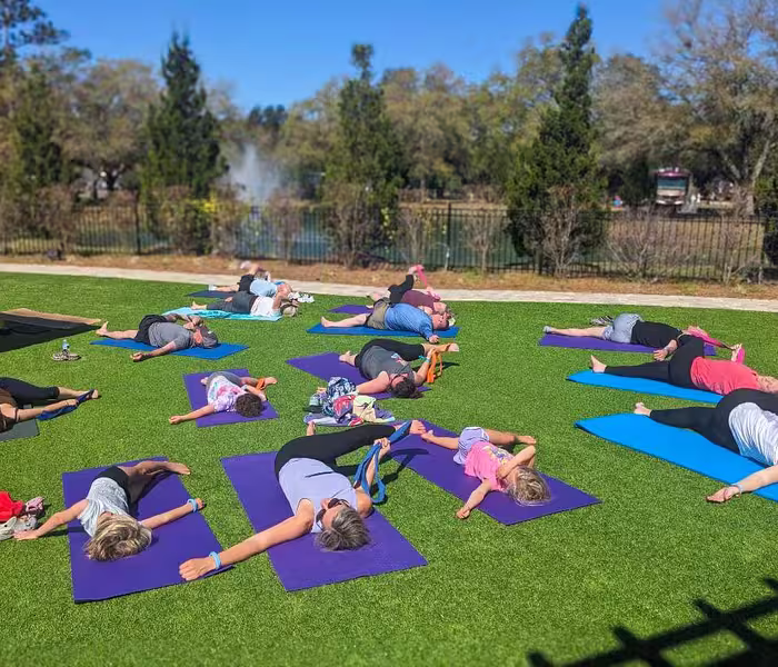 A group doing outdoor yoga on a green lawn with a lake view at Splash RV Resort in Milton, Florida