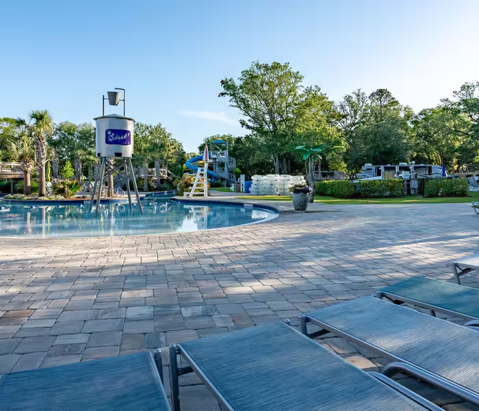 Splash RV Resort pool area with lounge chairs, water slide, and water tower on a sunny day.