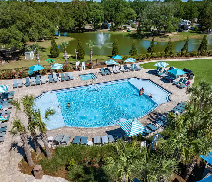 Aerial view of Splash RV Resort sparkling pool with striped umbrellas lounge chairs and palm trees with lake and fountains in background