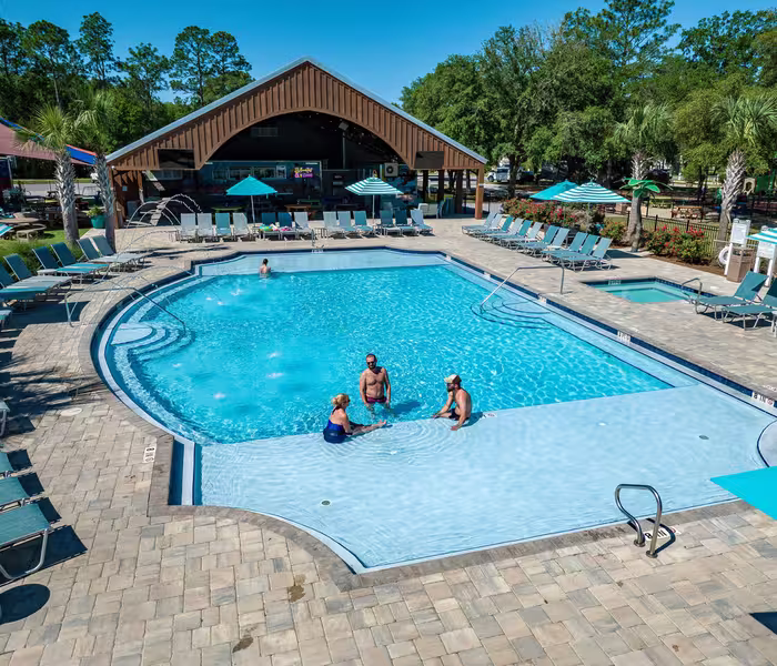 Guests relax in the resort pool and shallow wading area at Splash RV Resort, with lounge chairs and a large pavilion in the