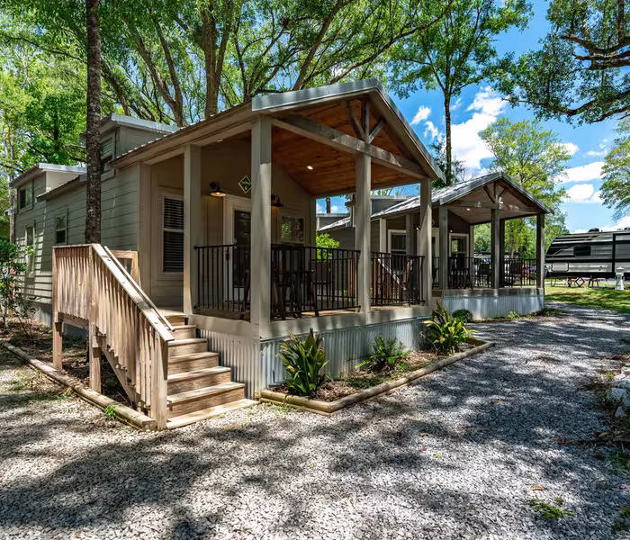 Sage-green luxury cottage exterior with covered front porch and oak trees at Splash RV Resort in Milton, Florida.