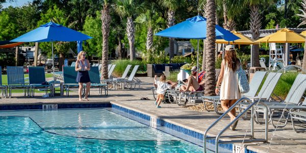 Guests relax by the swimming pool at Splash RV Resort surrounded by palm trees and lounge chairs.