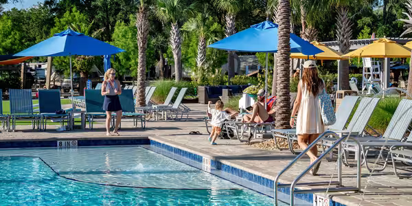 Guests relax by the swimming pool at Splash RV Resort surrounded by palm trees and lounge chairs.