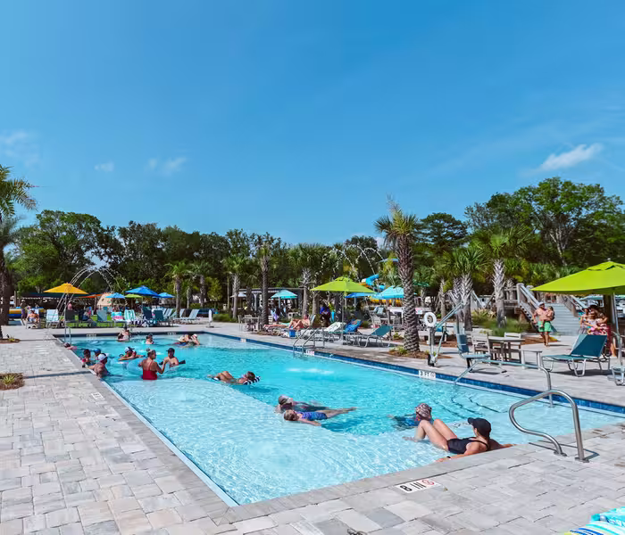 Guests enjoying the swimming pool at Splash RV Resort on a sunny day with lounge chairs and palm trees.