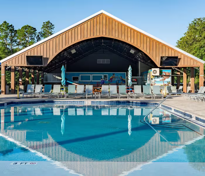 Large swimming pool at Splash RV Resort reflecting the wooden pavilion and lounge chairs.