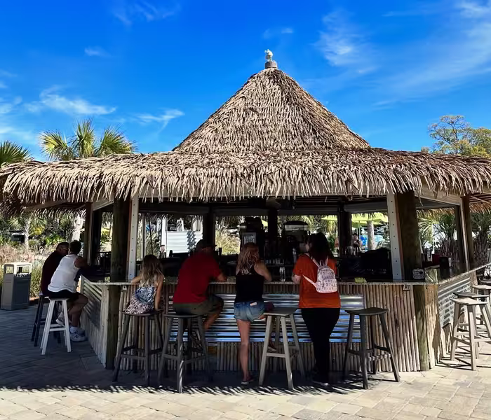 Guests gathered around thatched-roof tiki bar at Splash RV Resort in Milton, Florida on sunny day