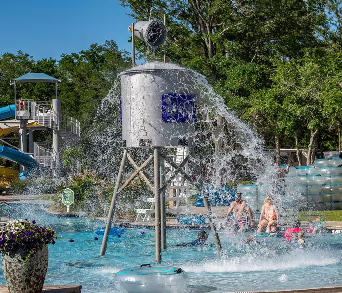 Guests enjoy the splash pad water playground at Splash RV Resort, featuring a giant tipping bucket and water slides.