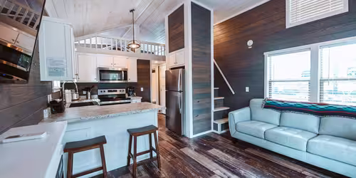 Modern glamping wagon interior at Splash RV Resort with a kitchen, sofa, and loft.