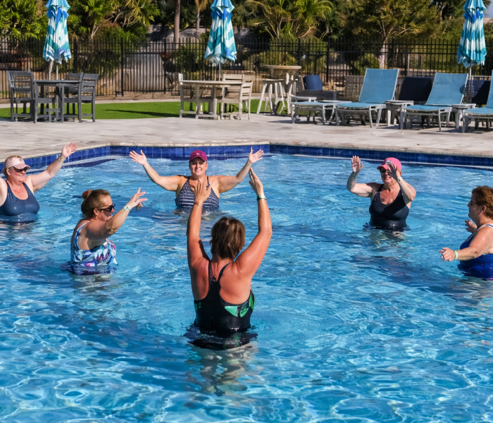 Women doing water aerobics in the resort swimming pool at Splash RV Resort, surrounded by lounge chairs and umbrellas.